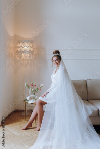 Morning preparations of a beautiful, sexy bride in a bathrobe on the balcony and on the sofa, where she puts on shoes in a wedding dress
