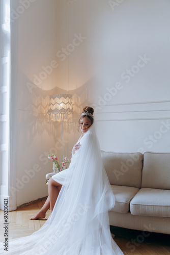 Morning preparations of a beautiful, sexy bride in a bathrobe on the balcony and on the sofa, where she puts on shoes in a wedding dress
