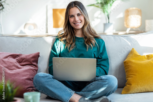 Beautiful kind woman working with laptop while sitting on couch in living room at home