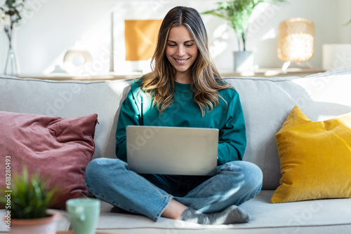 Beautiful kind woman working with laptop while sitting on couch in living room at home photo