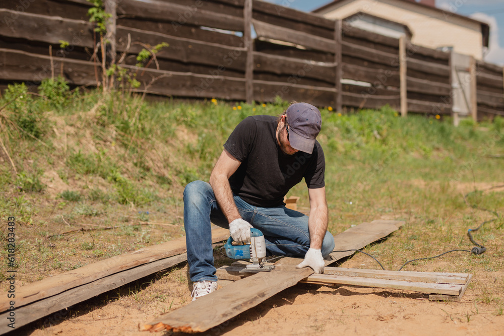 Male carpenter repairing a wooden fence - domestic rough male chores - manual labor Male carpenter repairing a wooden fence - domestic rough male chores - manual labor