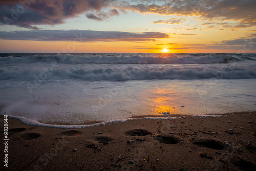 Long exposure of foot prints and waves washing onto a sandy during sunset.