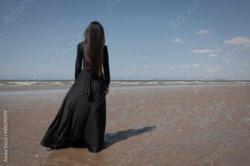 fine art rear view of woman in classic black dress on beach near ocean