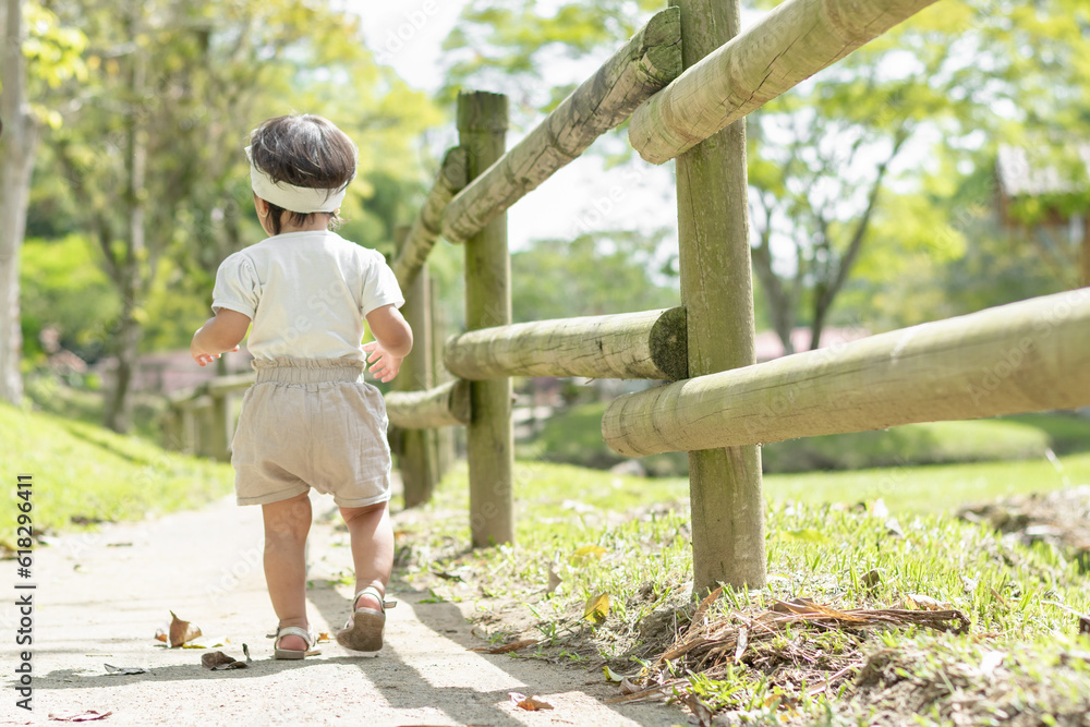 little latin girl walking along a path next to a wooden fence, in the middle of the green nature in a park.