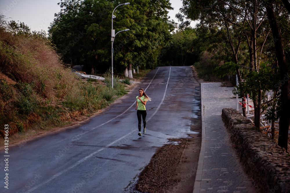 Young woman in sportswear is jogging early in morning on green track at sunrise. Pursuit of goals Young woman in sportswear is jogging early in morning on green track at sunrise. Pursuit of goals
