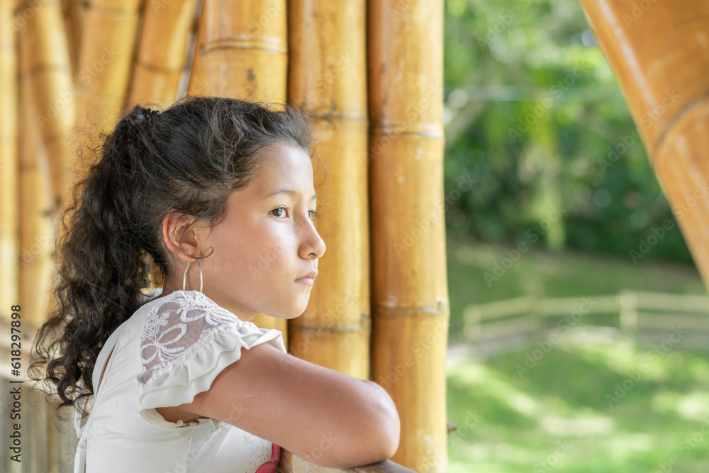 Little Latina girl with brown skin, very serious and bored, thinking about the bullying she receives, standing on the bamboo bridge. Little Latina girl with brown skin, very serious and bored, thinking about the bullying she receives, standing on the bamboo bridge.