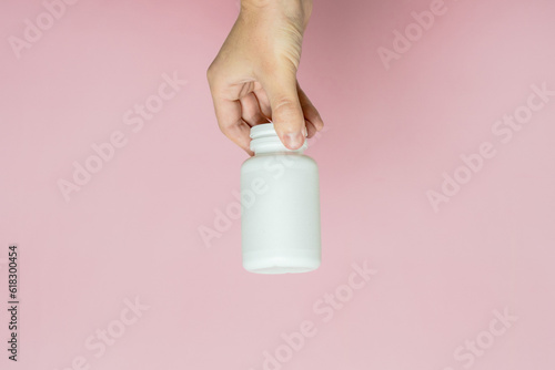 Woman's hand holding bottle of pills or vitamins. White packaging for your pill or capsule and supplement
