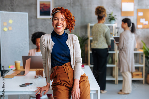 Obraz na plátne Portrait of young Hispanic business woman sitting on company office desk with coworkers in background