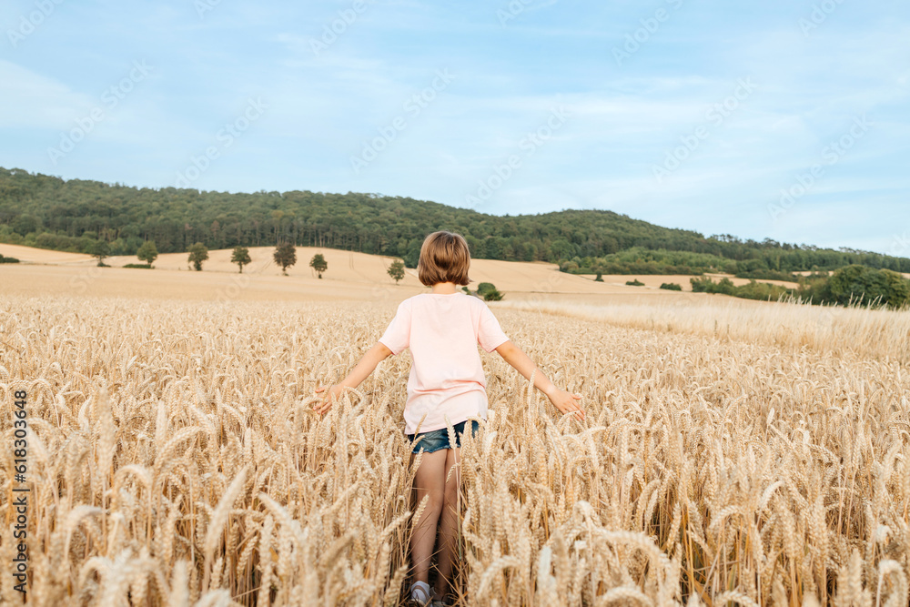 A happy school-age girl walks through a field of mature spikelets. Country life. summer holiday vacation. Vacation concept.