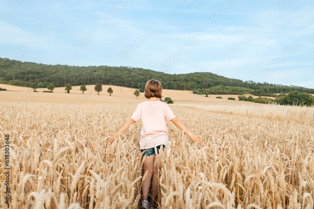 A happy school-age girl walks through a field of mature spikelets. Country life. summer holiday vacation. Vacation concept. A happy school-age girl walks through a field of mature spikelets. Country life. summer holiday vacation. Vacation concept.