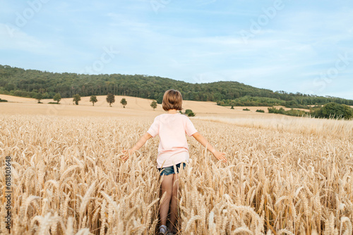 A happy school-age girl walks through a field of mature spikelets. Country life. summer holiday vacation. Vacation concept. © Elena Medoks