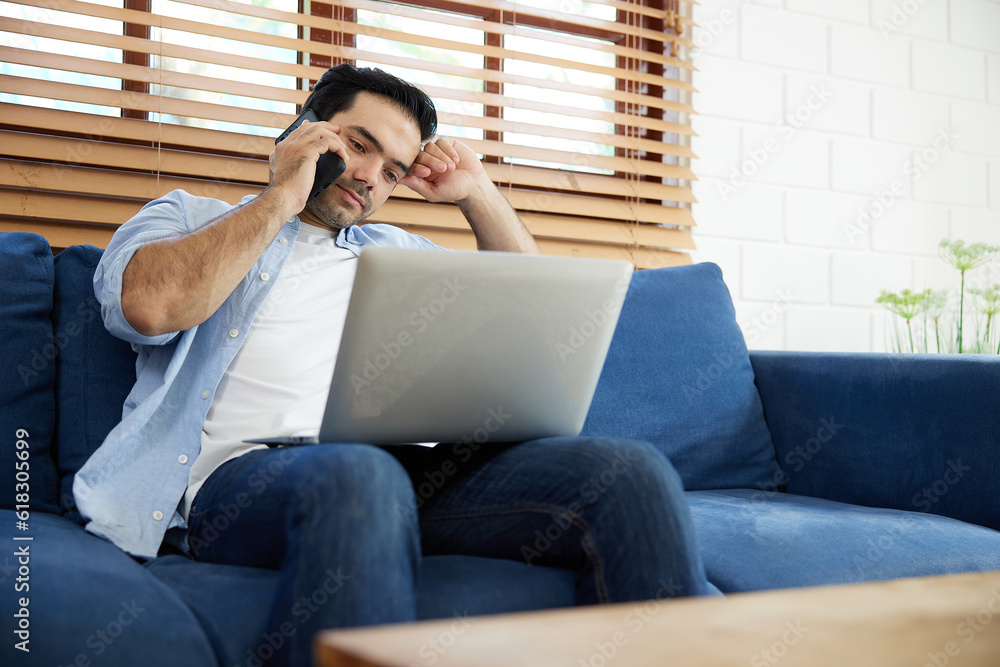 Fototapeta premium young handsome man using laptop computer and talking by smartphone at home