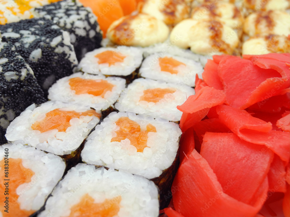 Assorted sushi set with baked soft cheese and flying fish caviar covered roll, maki sushi with salmon and pickled ginger in front. Japanese food background. Assorted sushi set with baked soft cheese and flying fish caviar covered roll, maki sushi with salmon and pickled ginger in front. Japanese food background.