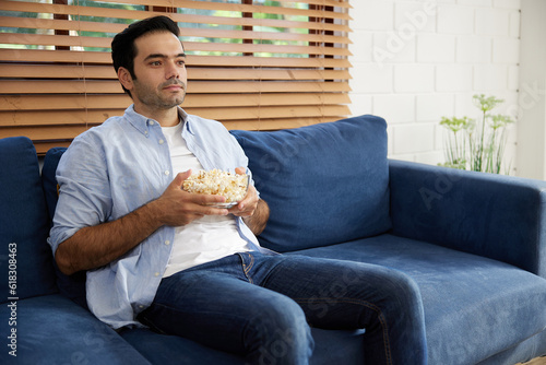 young handsome man watching movies and eating popcorn in a living room