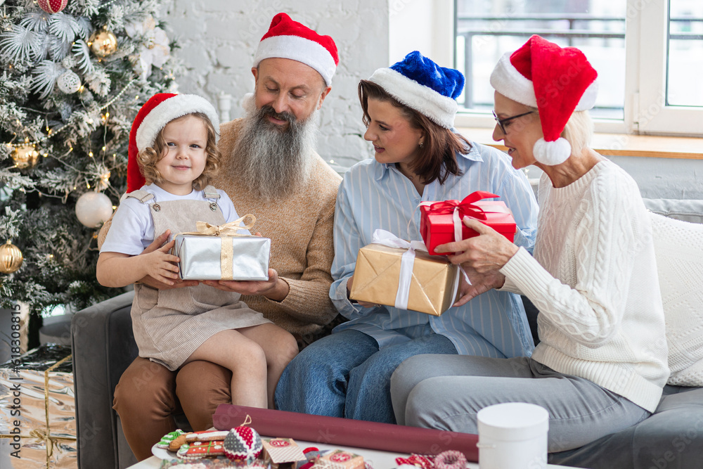 Fototapeta premium Happy smiling family near beautiful Christmas new year tree exchanging gifts in the morning. Grandmother, grandfather, daughter and granddaughter celebrating holidays at home together. 