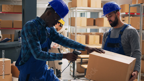 Diverse employees examining packs of goods in depot space, scanning barcodes on boxes to do inventory for shipment. Worker and manager in overalls working with retail merchandise.