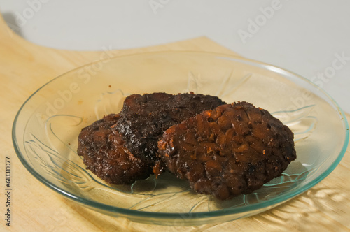 Three pieces of tempe bacem are served on a small plate on a wooden board isolated on a white background. photo