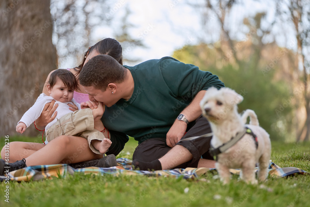 Fototapeta premium young couple having a picnic sitting on the grass and tickling their baby's feet