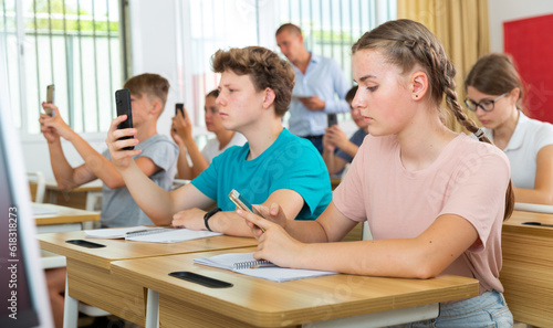 Teenager students sitting in class room with smartphones and photographing something.