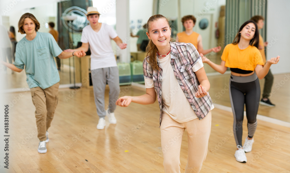 Smiling teenage girl dancer practicing active vigorous dance with group in modern studio.