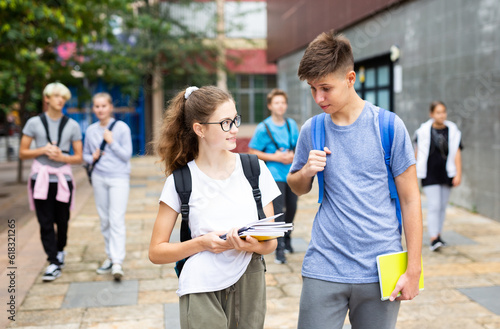Portrait of teen female and male schoolmates with backpacks and workbooks walking to college campus on warm autumn day.