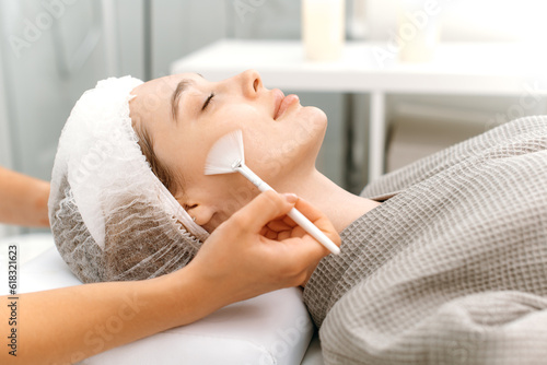 Side view at of a beautiful caucasian woman and a beautician cleaning the face with special gel before applying a mask, peeling, scrub. Facial skin care procedures in a beauty salon