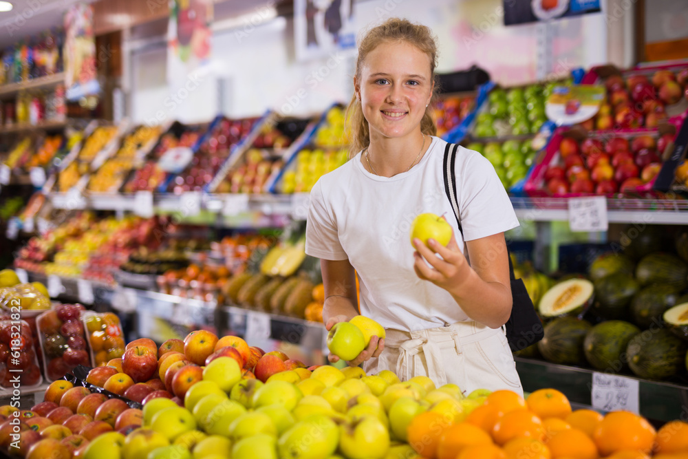 Fifteen-year-old girl who came to the store chooses ripe apples on the counter to buy them