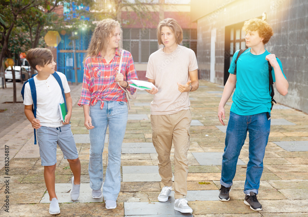 Group of positive cheerful teenagers hanging out on streets of city on summer day