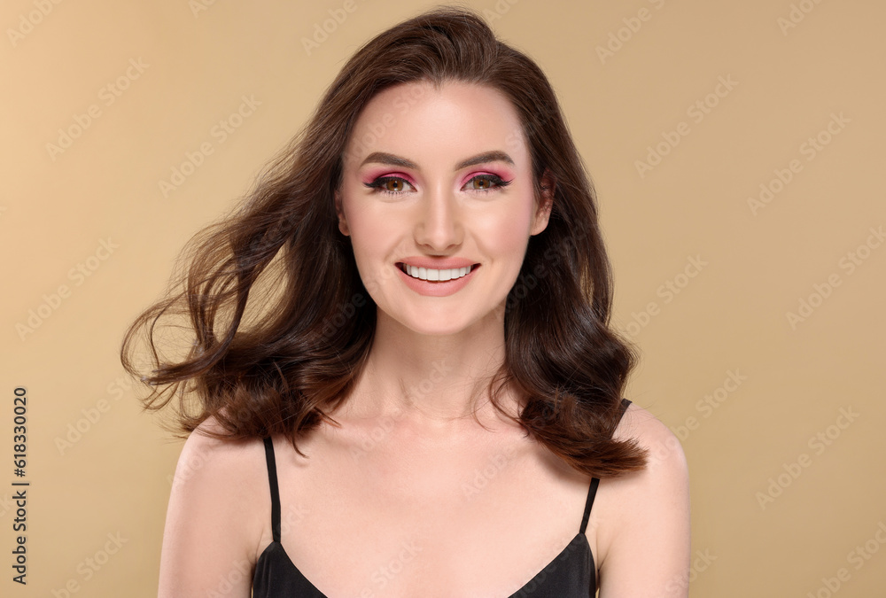 Portrait of beautiful young woman with makeup and gorgeous hair styling on beige background