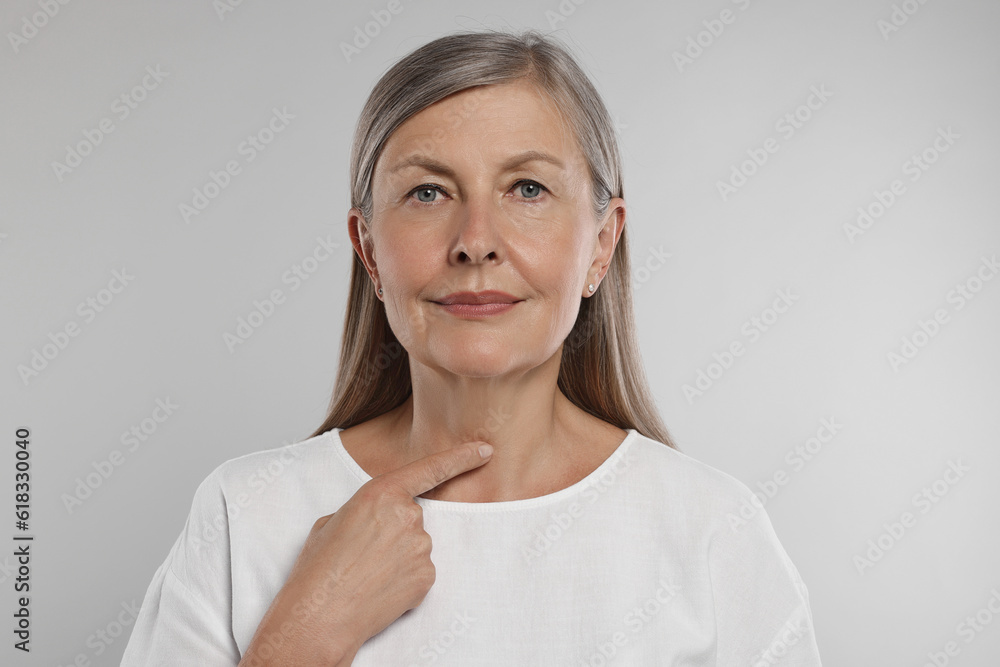 Endocrine system. Senior woman doing thyroid self examination on light grey background Endocrine system. Senior woman doing thyroid self examination on light grey background