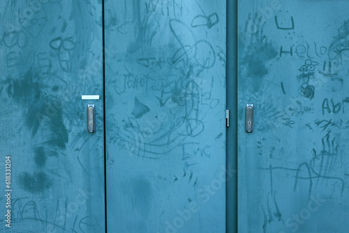Random graffiti marks on a teal blue public power station cupboard. Poorly hand drawn cock and ball or dick pics with names and illustrations. Vandalism & petty youth crime on public property concept