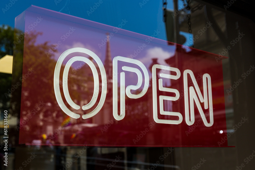 White neon open sign with a red background in a shop window