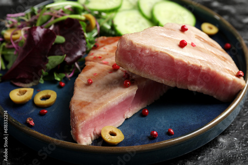 Pieces of delicious tuna with olives, salad and spices on plate, closeup