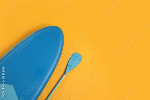 SUP board and paddle on yellow background, flat lay with space for text. Water sport