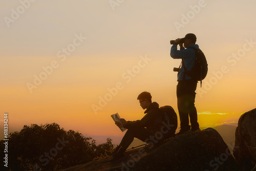 Two tourists with backpacks enjoying sunset on top of a mountain