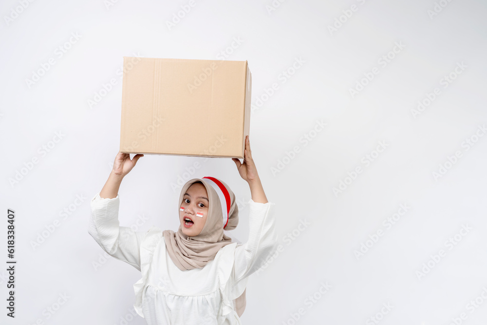 Cheerful Asian muslim woman celebrating indonesian independence day carrying package box isolated on white background. Indonesian independence day on 17 august concept Cheerful Asian muslim woman celebrating indonesian independence day carrying package box isolated on white background. Indonesian independence day on 17 august concept