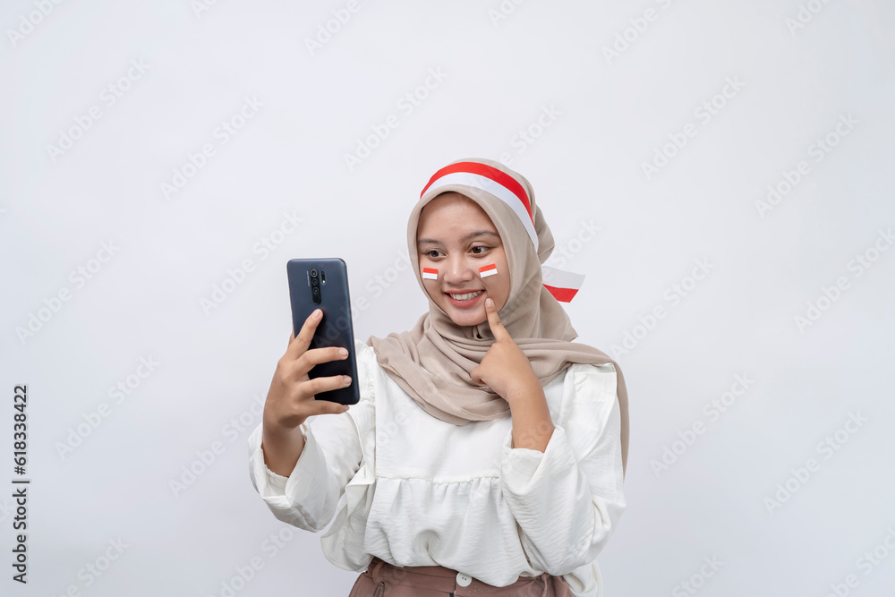Excited cute Asian women muslim holding mobile phone and celebrating indonesian independence day on 17 august isolated on white background Excited cute Asian women muslim holding mobile phone and celebrating indonesian independence day on 17 august isolated on white background