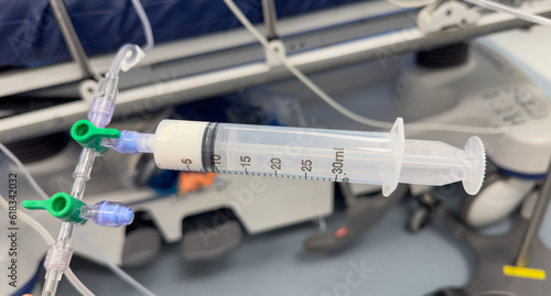hand holds a syringe amidst IV drips and medications, symbolizing medical care, treatment, and the use of drugs in a hospital setting