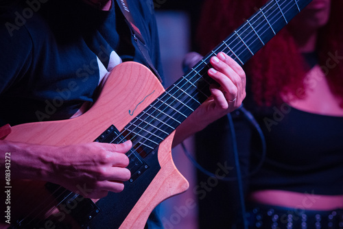 A portion of a guitar with the hands of the guitarist prominently featured, during the performance of a song, at night. Selective focus.