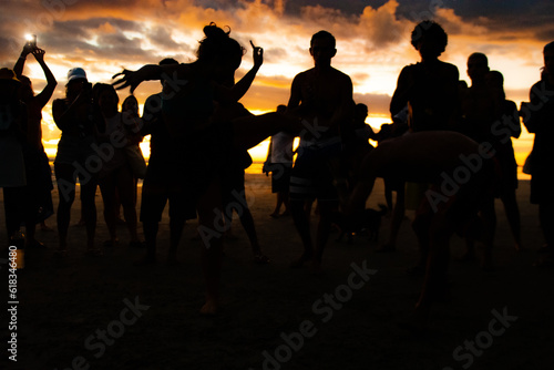 Capoeira wheel on the beach, silhouettes of participants at sunset. Featured Brazilian girl participating in capoeira circle.