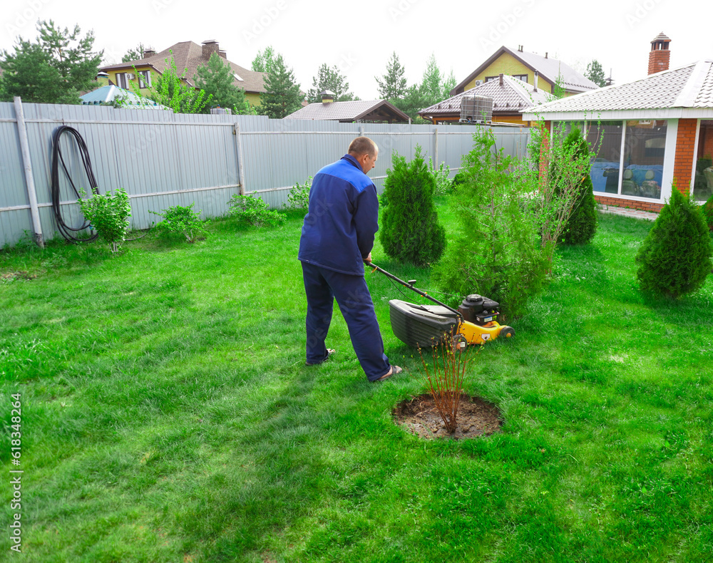 The man is working in the garden. Mowing grass with a lawn mower. The man is working in the garden. Mowing grass with a lawn mower.