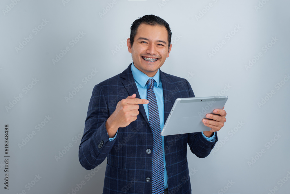young businessman smiles at camera with raised finger and a tablet, real estate seller young businessman smiles at camera with raised finger and a tablet, real estate seller