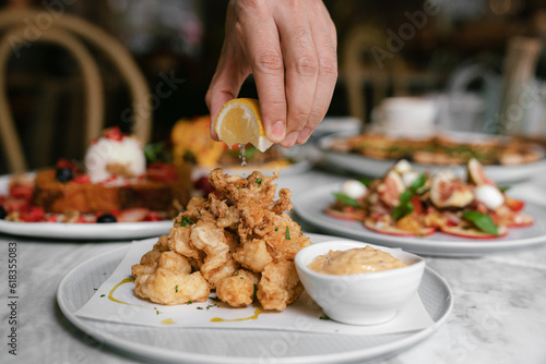 Canvastavla Squeezing lemon over deep fried calamari seafood on plate in restaurant
