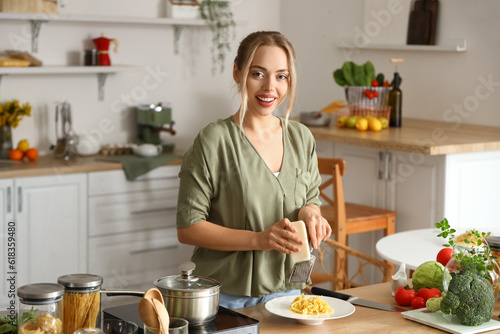 Young woman grating cheese on tasty pasta in kitchen