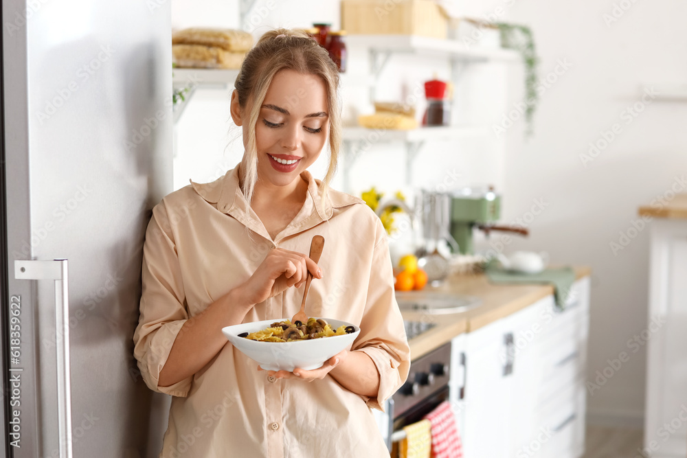 Young woman eating tasty pasta in kitchen