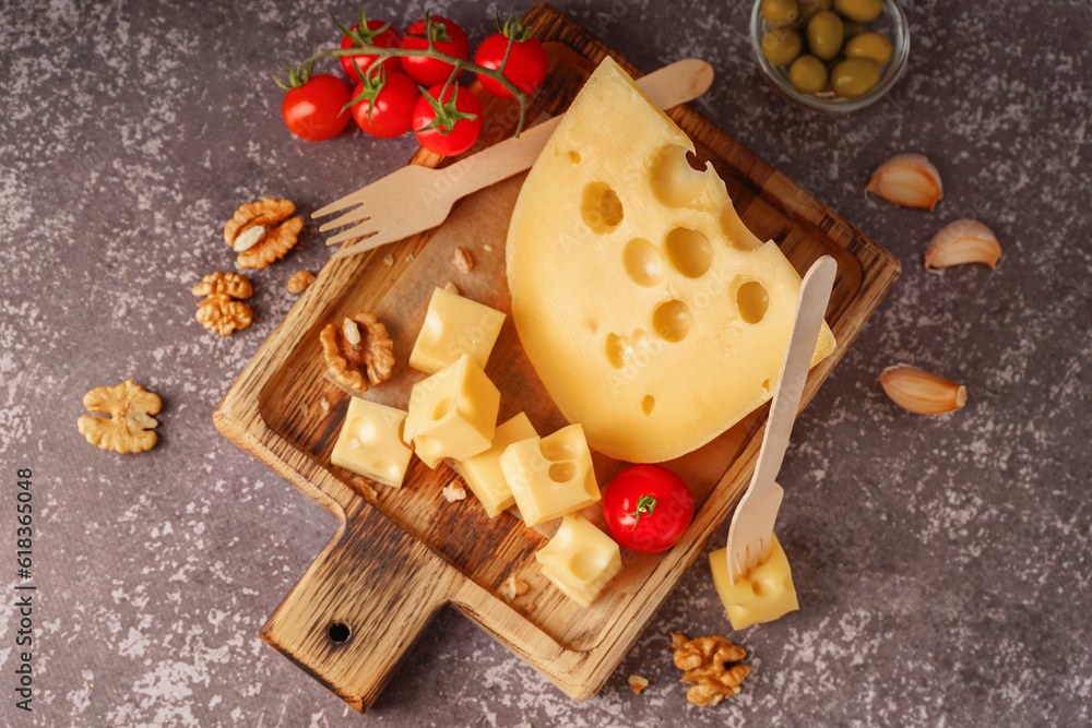 Board with pieces of Swiss cheese and tomatoes on grey background