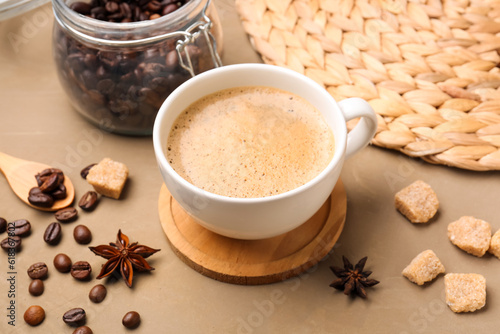 Cup of hot espresso and jar with coffee beans on brown background