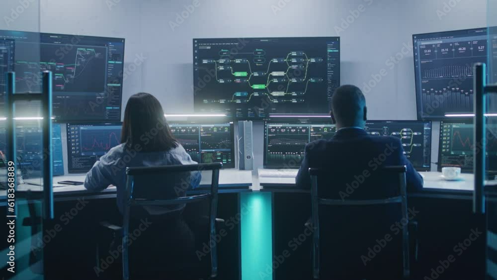 Diverse software engineers work on computers with database server. Administrator enters modern monitoring office, works with real-time analysis charts and blockchain network on big digital screens. Diverse software engineers work on computers with database server. Administrator enters modern monitoring office, works with real-time analysis charts and blockchain network on big digital screens.