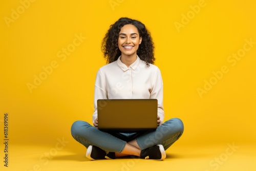 Smiling attractive young woman sitting on the floor with her legs crossed holding a laptop computer