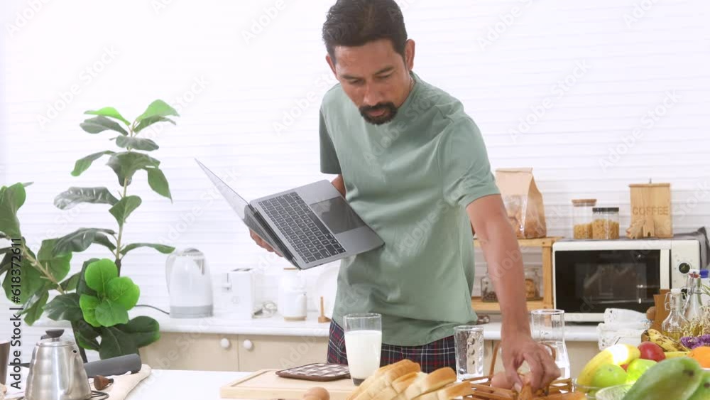 Hungry man focus on laptop walking into kitchen to find cookies to eat while working or meeting early morning, Asian busy male refuses breakfast because of pending work. Bachelor man lifestyle concept Hungry man focus on laptop walking into kitchen to find cookies to eat while working or meeting early morning, Asian busy male refuses breakfast because of pending work. Bachelor man lifestyle concept